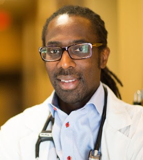 A person with glasses, wearing a white coat and a stethoscope around their neck, smiles at the camera.